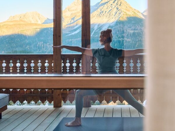 Carmen Gründerin von Soulbase, macht Yoga auf der Terrasse vom BelArosa Charlet. Hierbei trägt sie ein Türkises Yogaoutfit. Im Hintergrund sieht man die Berge bei Sonnenuntergang