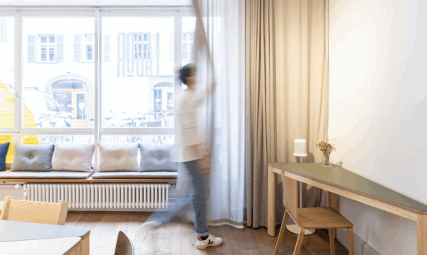 Das Labor in der Pfistergasste in Chur ist ein Eventraum. Das Bild zeigt wie jemand die Vorhänge der grossen Fenster öffnet und so Tageslicht in den hellen modernen Raum lässt.