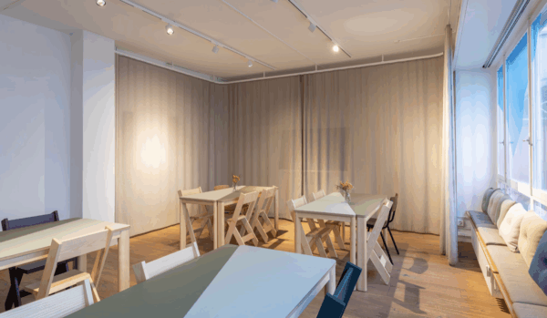 Das Labor, ein heller modern eingerichteter Eventraum in der Altstadt in Chur. Es hat grosse helle Fenster und ist in Grün/Beige dekoriert. Auf dem Bild sehen wir Tischinseln mit entsprechenden Stühlen